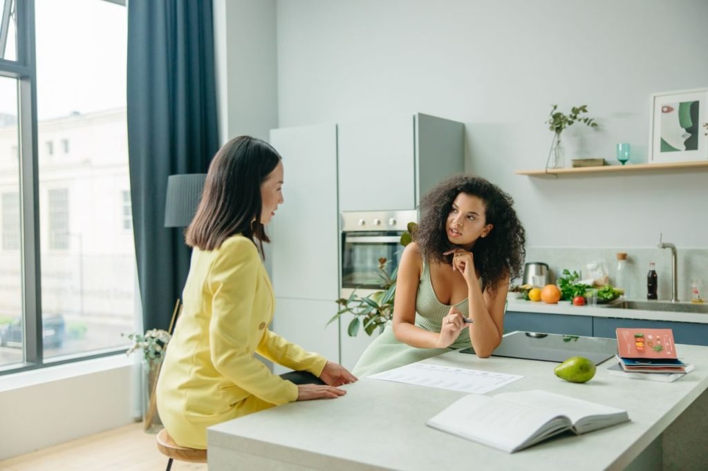 food-man-love-people-8844891 Two women engage in a conversation about nutrition in a stylish kitchen setting.