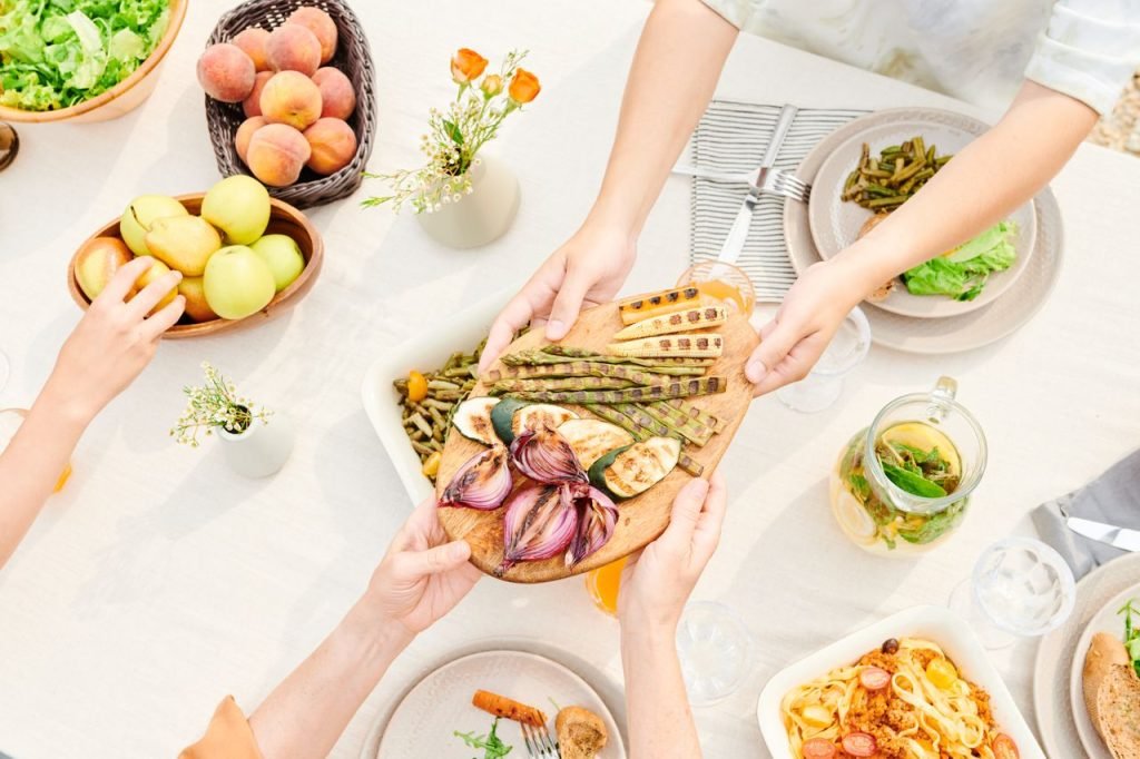 hands-passing-a-platter-of-veggies-8841217 Overhead view of a family sharing a meal with fresh grilled vegetables and fruits, perfect for a healthy lifestyle.